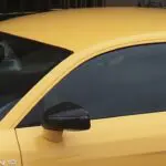 Bright yellow sports car with dark tinted windows and black side mirror parked in driveway