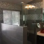 Modern bathroom with gray herringbone tile walls, frameless glass shower enclosure, white subway tile surround, and vanity with mirror and lighting fixtures