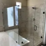Frameless glass shower enclosure with marble tile surround and window with blinds