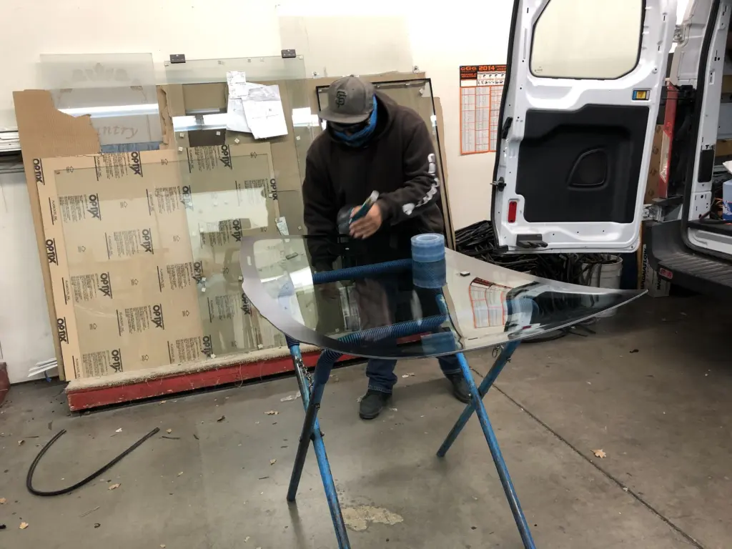 A Z-1 Glass technician working on a curved auto glass panel on a stand in the shop