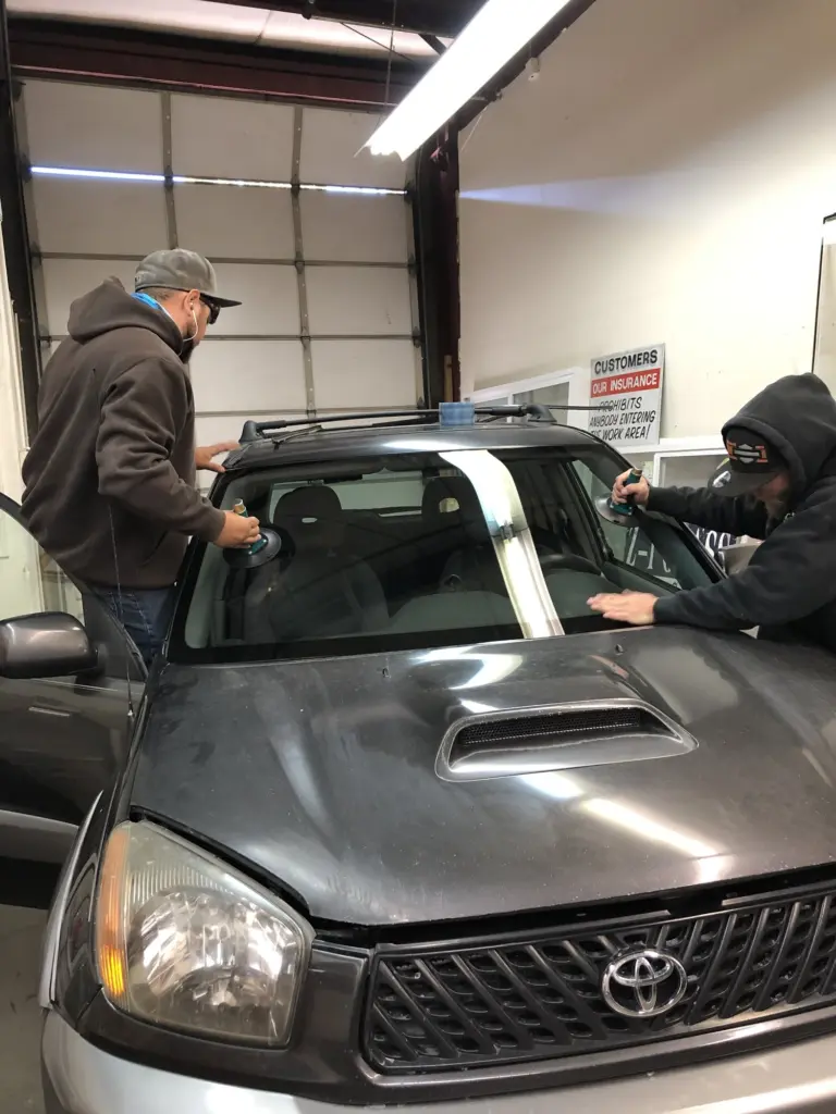 Two Z-1 Glass technicians setting a new windshield on a gray Toyota in the shop